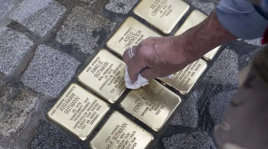 Gunter Demnig, fundador del proyecto Stolpersteine, limpia las también denominadas "piedras de tropiezo", recién colocadas en conmemoración de la familia Gutmann en Feuchtwangen, Baviera. (AFP)