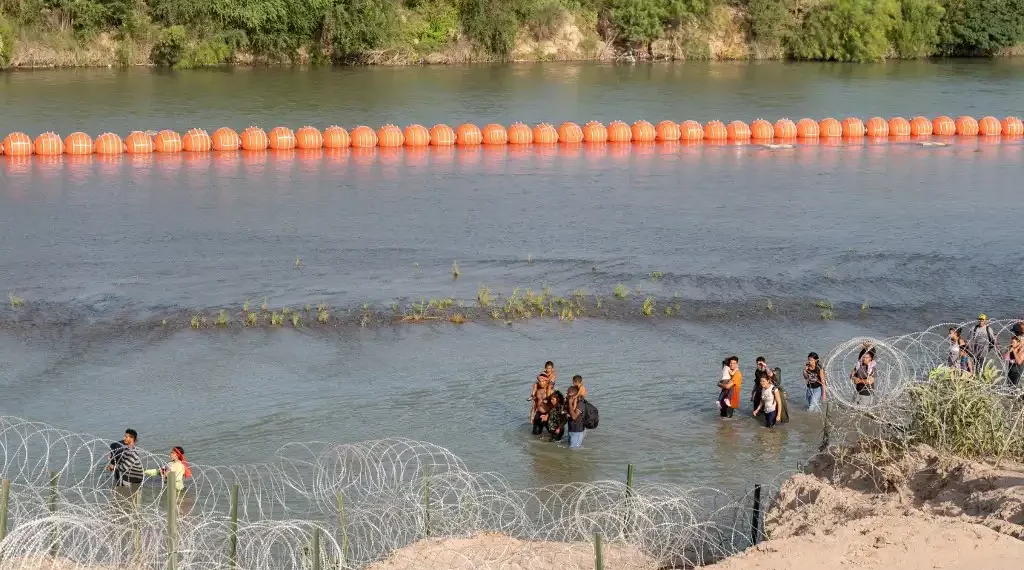 Migrantes caminan junto a una serie de boyas colocadas en el agua a lo largo de la frontera de Río Grande con México, en Eagle Pass, Texas. (AFP)
