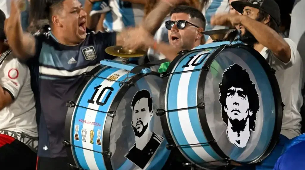 Los rostros de la leyenda del futbol argentino Diego Maradona (derecha) y el delantero Lionel Messi se ven en los tambores de los fanáticos de Argentina antes del inicio de un partido de futbol. (AFP)