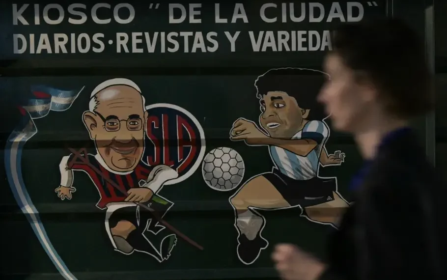 Una mujer pasa junto a un quiosco con pinturas que representan al difunto papa Francisco (izquierda), vestido como un jugador del San Lorenzo, y la leyenda del futbol Diego Maradona, cerca de la Catedral de Buenos Aires. (AFP)