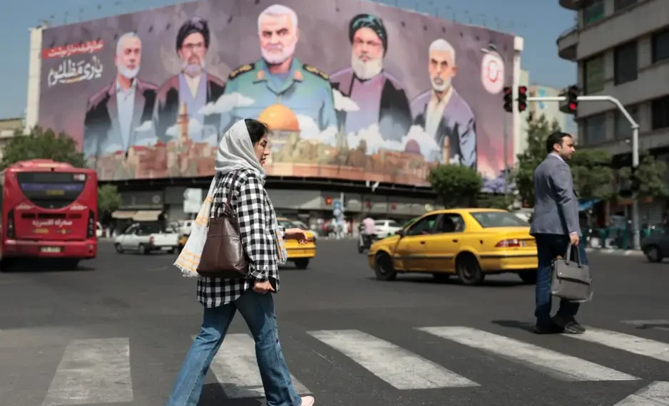 Una mujer pasa junto a una valla publicitaria con los retratos de los líderes iraníes y libaneses asesinados en la plaza Enghelab de Teherán. (AFP)