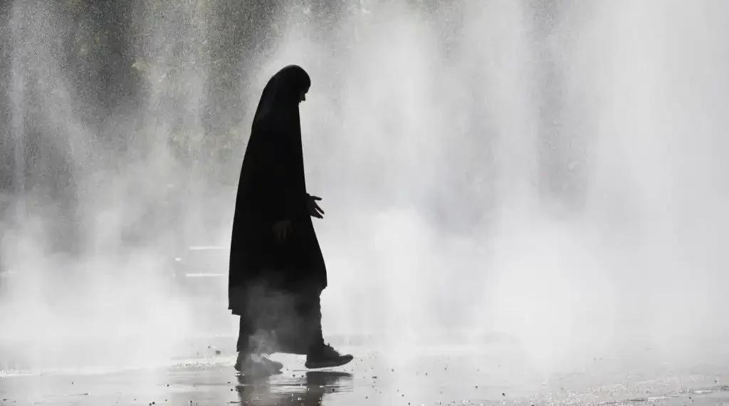 Una mujer con hiyab camina entre las salpicaduras de agua de una fuente. (AFP)