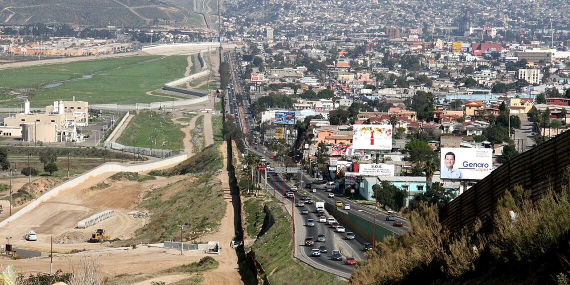 Vista aérea del muro fronterizo entre Tijuana, México, y San Diego, California, tomada desde el lado estadounidense. El muro se extiende a lo largo del terreno montañoso, simbolizando la división física y política entre ambos países.