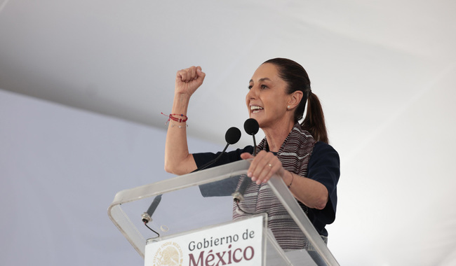 Claudia Sheinbaum levanta el puño y sonríe mientras da un discurso desde un podio con el emblema del Gobierno de México.